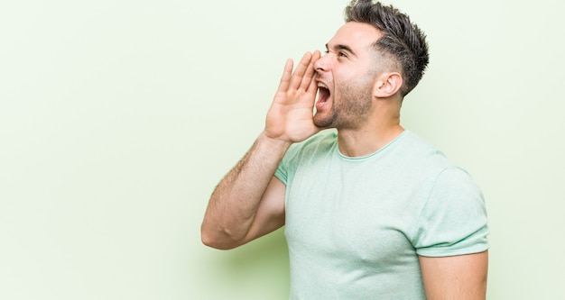 Giovane uomo bello contro un verde che grida e che tiene la palma vicino alla bocca aperta.