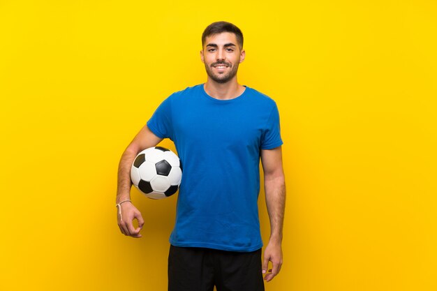 Giovane uomo bello del giocatore di football americano sopra la parete gialla isolata che sorride molto