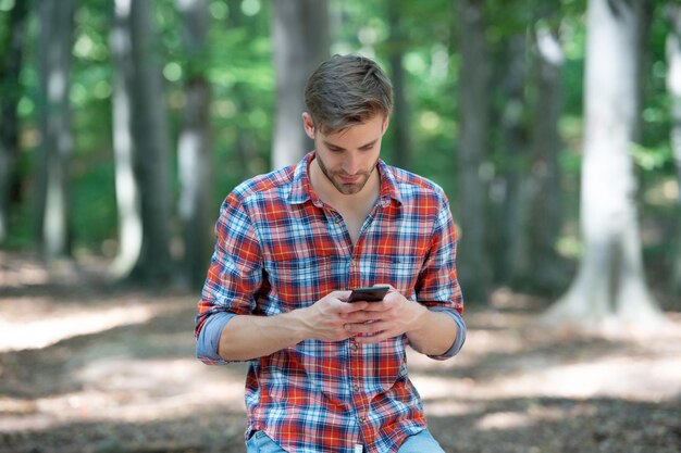 Giovane uomo bello in camicia a scacchi chat sul telefono all'aperto