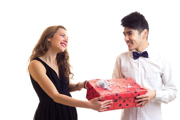 Giovane uomo bello in camicia bianca con papillon nero e giovane bella donna che tiene regalo rosso