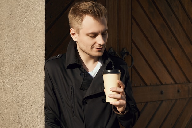 Giovane uomo bello in cappotto scuro con una tazza di caffè