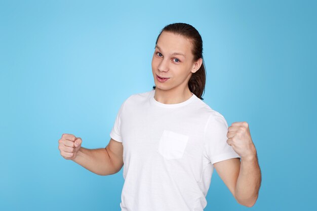 Giovane uomo bello in t-shirt che mostra gesto di vittoria isolato su sfondo blu.