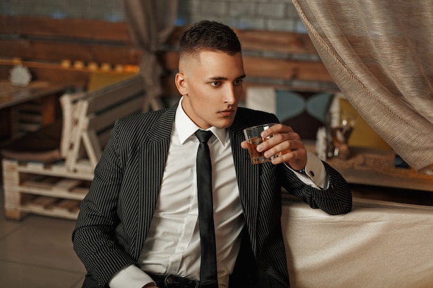 Giovane uomo bello in un vestito elegante, bere whisky