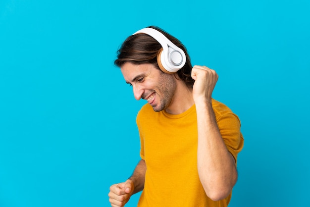 Giovane uomo bello isolato sulla parete blu ascoltando musica e balli