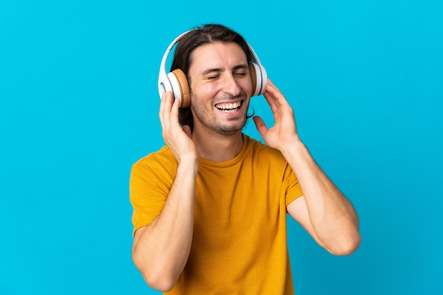 Giovane uomo bello isolato sulla parete blu che ascolta musica e canto