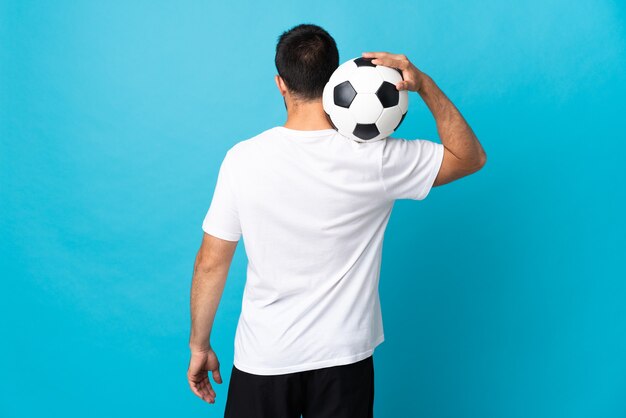 Giovane uomo bello isolato sulla parete blu con pallone da calcio