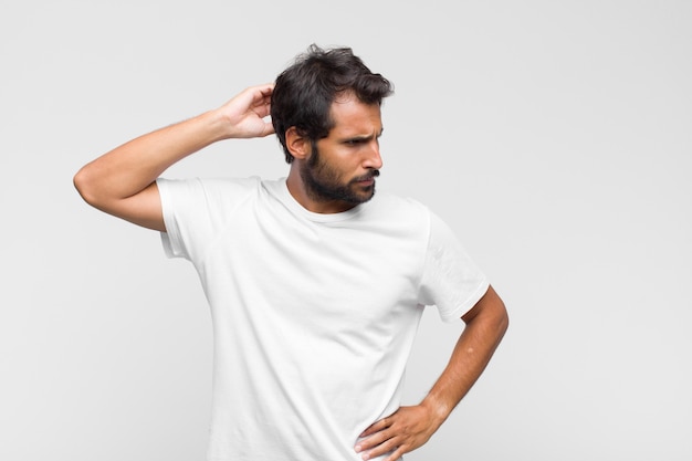 Giovane uomo bello latino che si sente perplesso e confuso, grattandosi la testa e guardando di lato