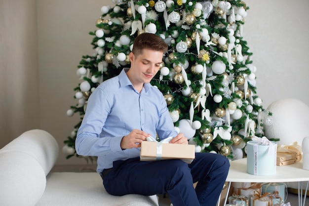 Giovane uomo bello seduto nel soggiorno e con in mano un regalo di Natale