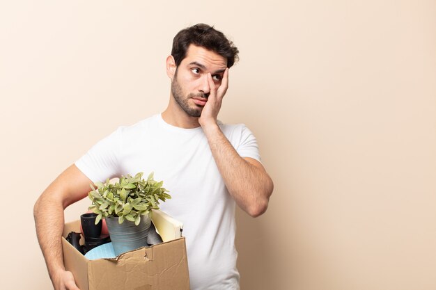 Giovane uomo bello sentirsi annoiato, frustrato e assonnato dopo un compito noioso, noioso e noioso, tenendo la faccia con la mano