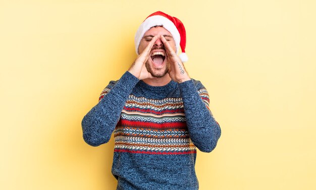 Giovane uomo bello sentirsi felice, dando un grande grido con le mani vicino alla bocca. concetto di natale