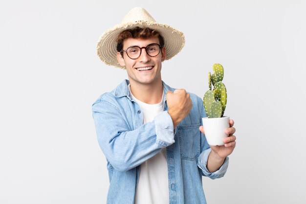 Giovane uomo bello sentirsi felice e affrontare una sfida o festeggiare. contadino con in mano un cactus decorativo