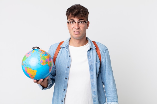 Giovane uomo bello sentirsi perplesso e confuso. studente con in mano una mappa del globo