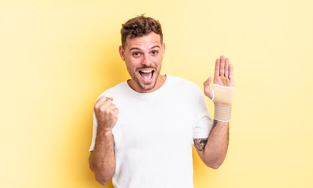 giovane uomo bello sentirsi scioccato, ridere e celebrare il successo. concetto di fasciatura per le mani