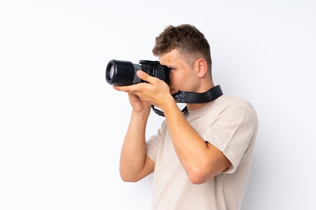 Giovane uomo bello sopra bianco isolato con una macchina fotografica professionale