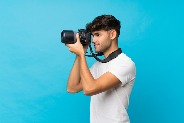 Giovane uomo bello sopra il blu isolato con una macchina fotografica professionale