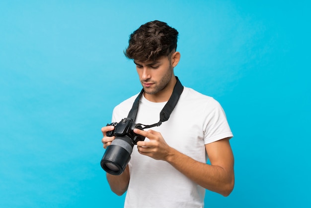 Giovane uomo bello sopra il blu isolato con una macchina fotografica professionale