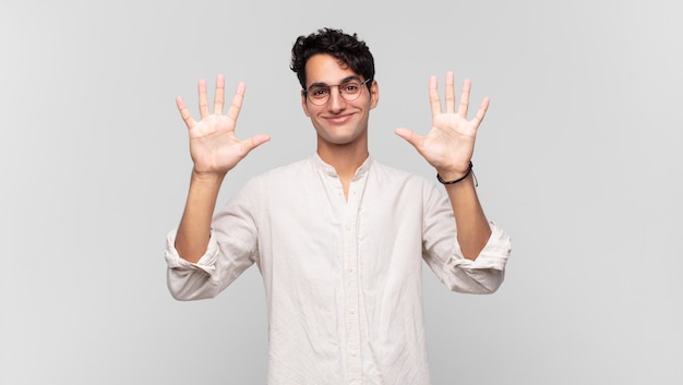 Giovane uomo bello sorridente e guardando amichevole, mostrando il numero dieci o decimo con la mano in avanti, conto alla rovescia