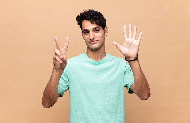 Giovane uomo bello sorridente e guardando amichevole, mostrando il numero sette o settimo con la mano in avanti, conto alla rovescia