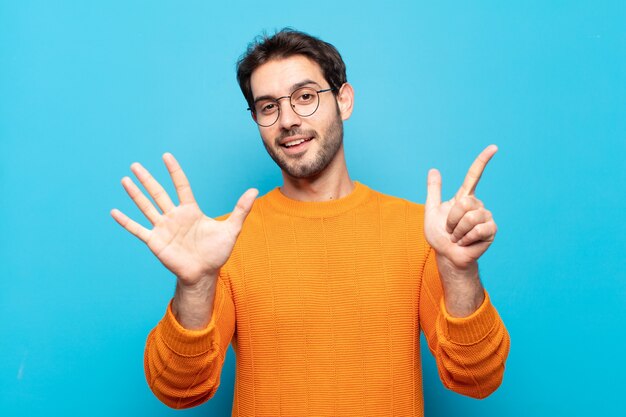 Giovane uomo bello sorridente e guardando amichevole, mostrando il numero sette o settimo con la mano in avanti, conto alla rovescia