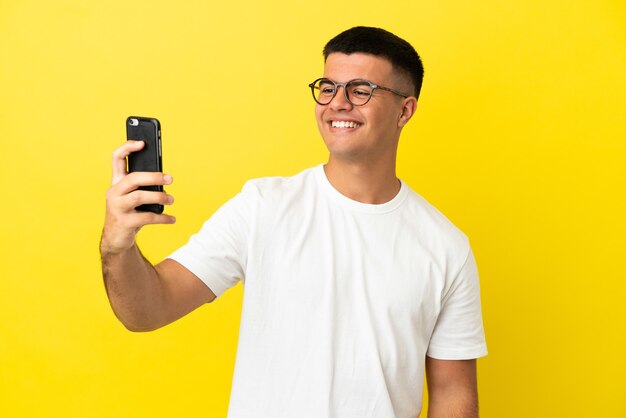 Giovane uomo bello su sfondo giallo isolato che fa un selfie