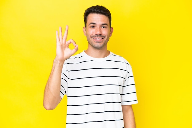 Giovane uomo bello su sfondo giallo isolato che mostra segno ok con le dita