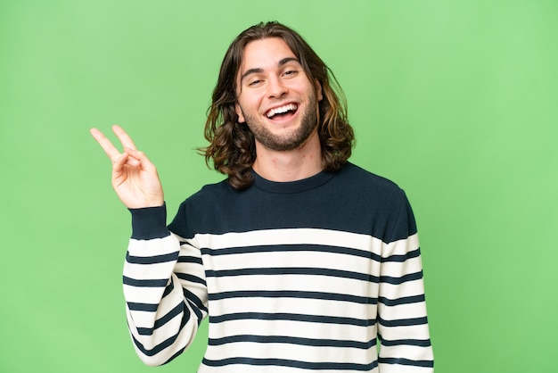 Giovane uomo bello su sfondo isolato sorridente e mostrando segno di vittoria