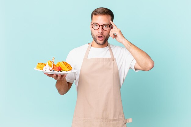 Giovane uomo biondo bello che sembra sorpreso, realizzando un nuovo pensiero, idea o concetto. cucinare il concetto di waffle