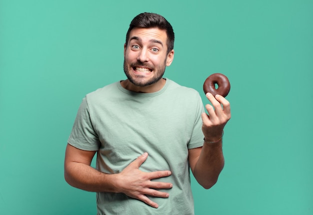 Giovane uomo biondo bello con una ciambella al cioccolato. concetto di colazione