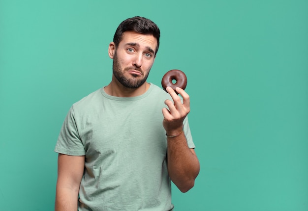 Giovane uomo biondo bello con una ciambella al cioccolato. concetto di colazione