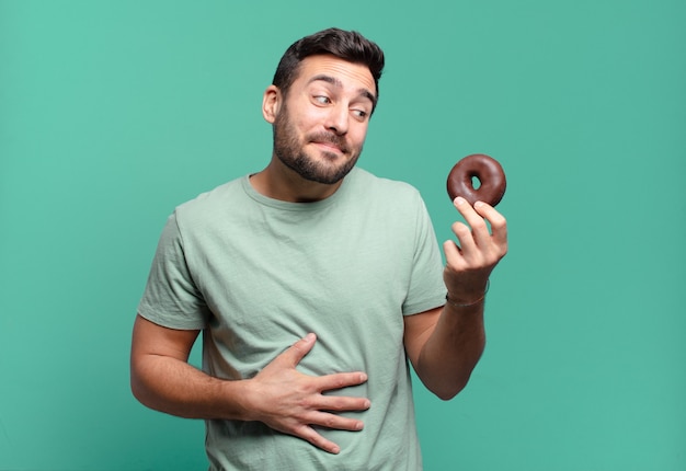 Giovane uomo biondo bello con una ciambella al cioccolato