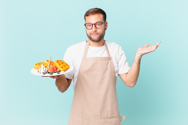 Giovane uomo biondo bello sentirsi perplesso, confuso e dubbioso. cucinare il concetto di waffle