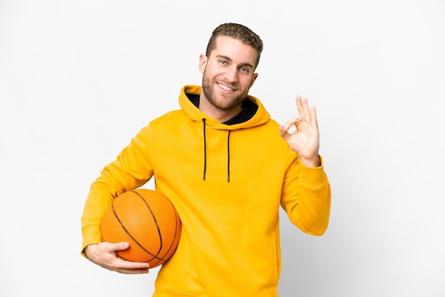 Giovane uomo biondo bello su sfondo bianco isolato giocando a basket e facendo segno OK