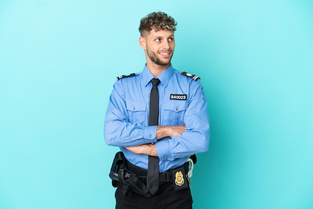 Giovane uomo biondo della polizia isolato bianco su sfondo blu guardando in alto mentre sorride