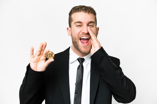 Giovane uomo biondo di affari che tiene un Bitcoin sopra fondo bianco isolato che grida con la bocca spalancata