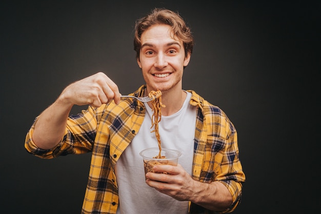 Giovane uomo biondo in camicia gialla che sorride e che tiene la forchetta degli spaghetti