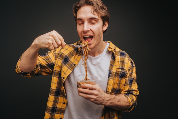 Giovane uomo biondo in camicia gialla che tiene la forchetta degli spaghetti prima di mangiare