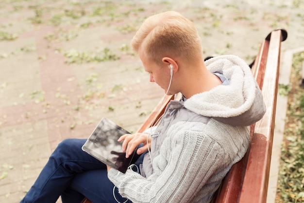 Giovane uomo biondo seduto e ascoltando musica con auricolari e tablet, concetto di stile di vita