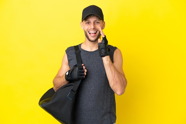 Giovane uomo biondo sportivo con borsa sportiva isolata su sfondo giallo che grida con la bocca spalancata