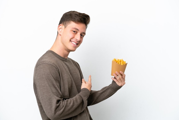 Giovane uomo brasiliano che tiene patatine fritte isolate su sfondo bianco che punta indietro