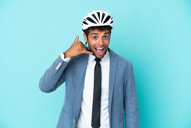 Giovane uomo brasiliano d'affari con casco da bici isolato su sfondo blu che fa il gesto del telefono Chiamami indietro segno