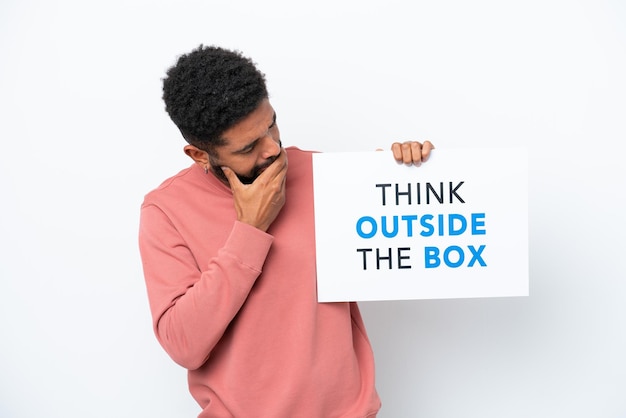 Giovane uomo brasiliano isolato su sfondo bianco con in mano un cartello con testo Think Outside The Box e pensiero