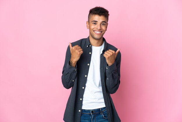 Giovane uomo brasiliano isolato sulla parete rosa che dà un pollice in alto gesto