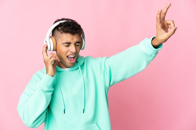 Giovane uomo brasiliano sopra musica d'ascolto della parete isolata con un mobile e cantando