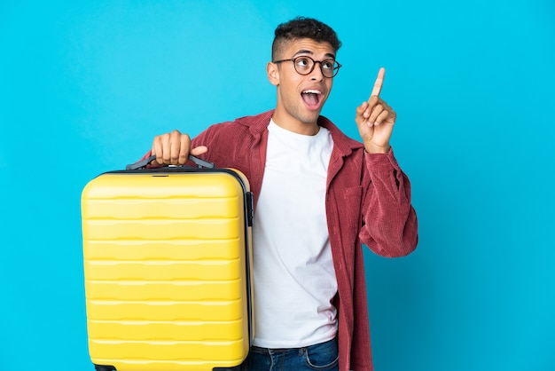 Giovane uomo brasiliano su sfondo isolato in vacanza con la valigia da viaggio e rivolto verso l'alto