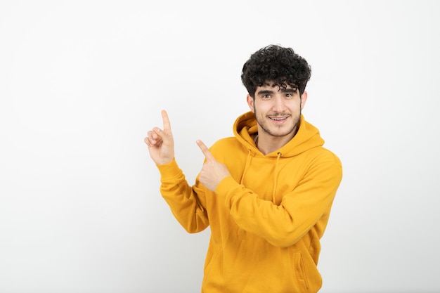 giovane uomo bruna in felpa con cappuccio gialla in piedi e indicando da parte.