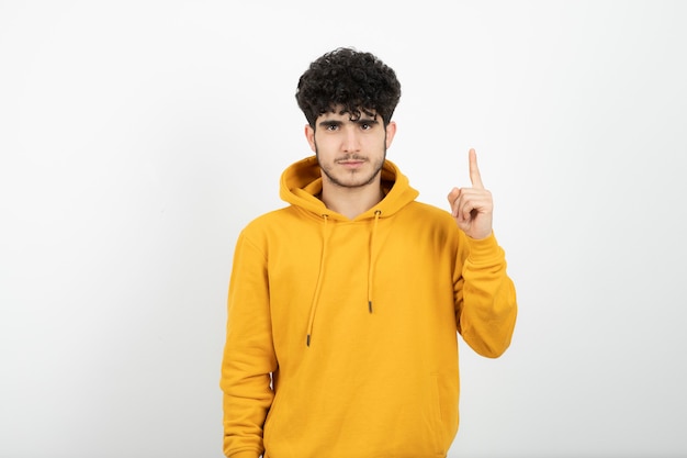 giovane uomo bruna in felpa con cappuccio gialla in piedi e rivolto verso l'alto il dito indice.