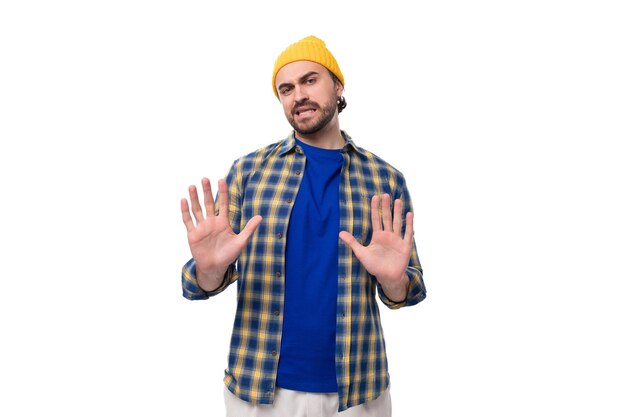 Giovane uomo bruno europeo dubbioso con barba e baffi vestito con un berretto giallo e un blu