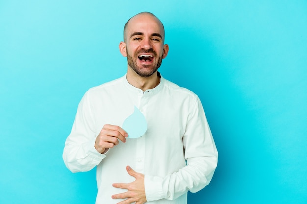 Giovane uomo calvo caucasico che celebra la giornata mondiale dell'acqua isolata sul blu ridendo e divertendosi.