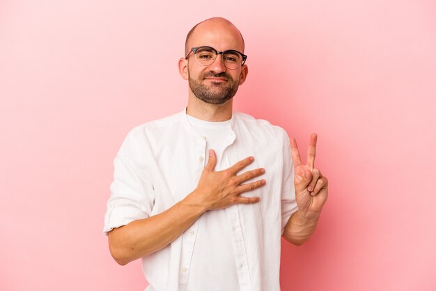 Giovane uomo calvo caucasico isolato su sfondo rosa prestando giuramento, mettendo la mano sul petto.