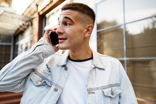 Giovane uomo casual che cammina per strada e parla al telefono vicino ritratto